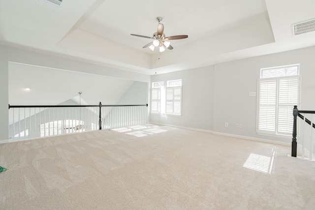 carpeted spare room featuring a raised ceiling, visible vents, a ceiling fan, and baseboards
