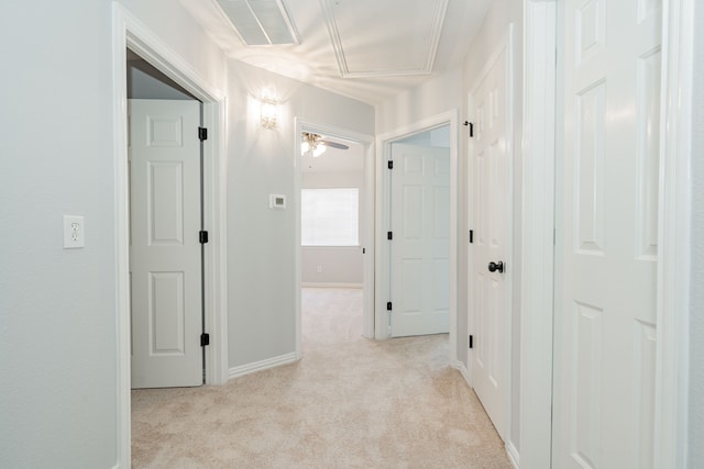 hallway with attic access, baseboards, light colored carpet, and visible vents