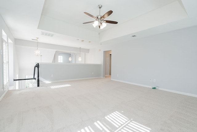 unfurnished room with carpet floors, a tray ceiling, visible vents, and baseboards