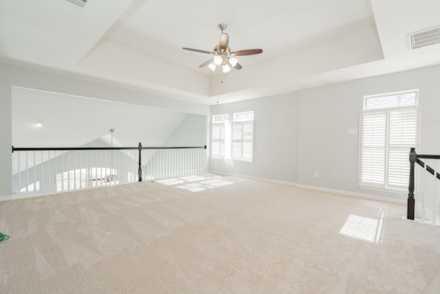 carpeted spare room featuring plenty of natural light, visible vents, a tray ceiling, and a ceiling fan