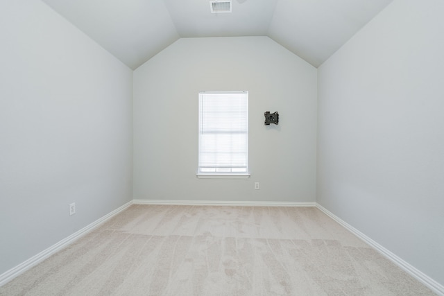 empty room featuring light colored carpet, visible vents, vaulted ceiling, and baseboards