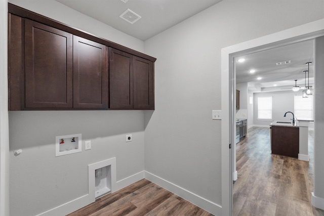 clothes washing area with hookup for a washing machine, cabinet space, hookup for an electric dryer, a sink, and wood finished floors