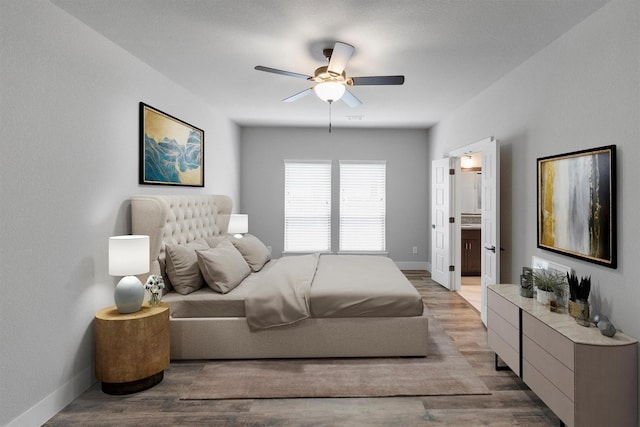 bedroom with baseboards, ensuite bath, a ceiling fan, and light wood-style floors