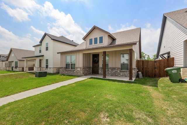 view of front of home featuring a shingled roof, brick siding, fence, board and batten siding, and a front yard