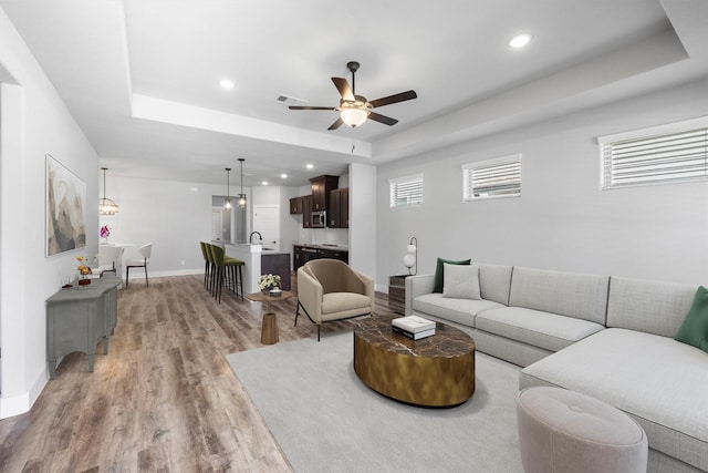 living area featuring light wood finished floors, visible vents, baseboards, a raised ceiling, and recessed lighting