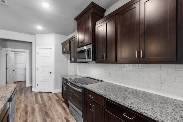 kitchen featuring light stone counters, stainless steel appliances, backsplash, dark brown cabinetry, and wood finished floors