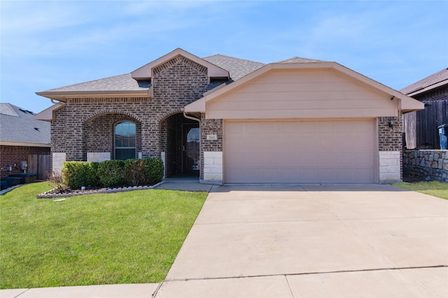 view of front facade with an attached garage, a shingled roof, a front lawn, and brick siding