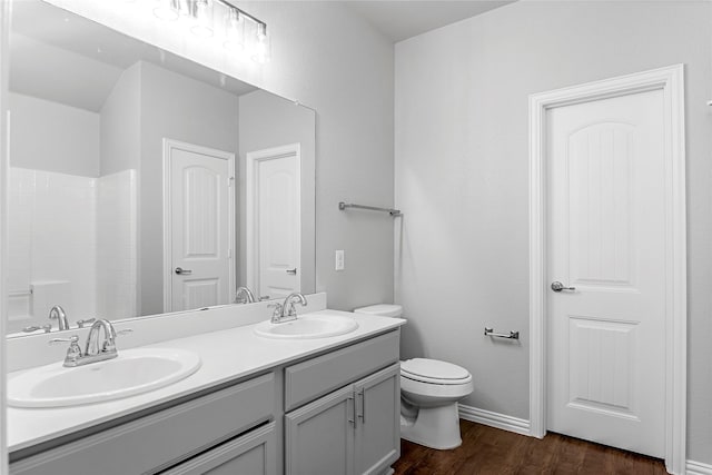 bathroom with double vanity, a sink, toilet, and wood finished floors