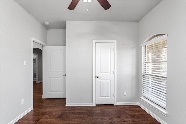 unfurnished bedroom featuring arched walkways, wood finished floors, and baseboards