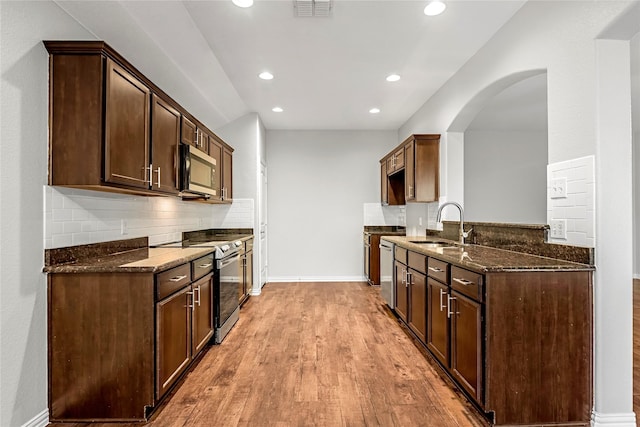 kitchen with stainless steel appliances, visible vents, decorative backsplash, a sink, and dark stone countertops