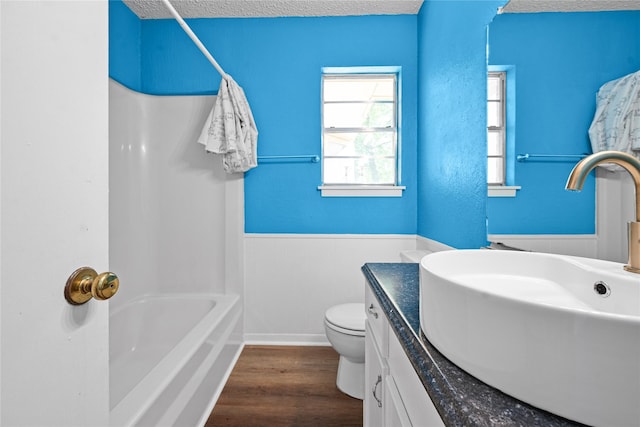 bathroom with vanity, wood finished floors, a textured ceiling, toilet, and a wainscoted wall