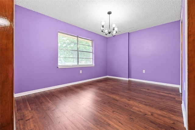 spare room with a chandelier, a textured ceiling, wood finished floors, and baseboards