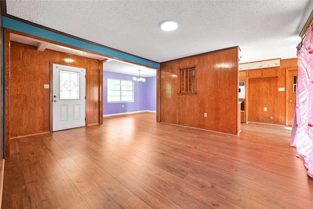 foyer entrance featuring a chandelier, wooden walls, a textured ceiling, wood finished floors, and baseboards