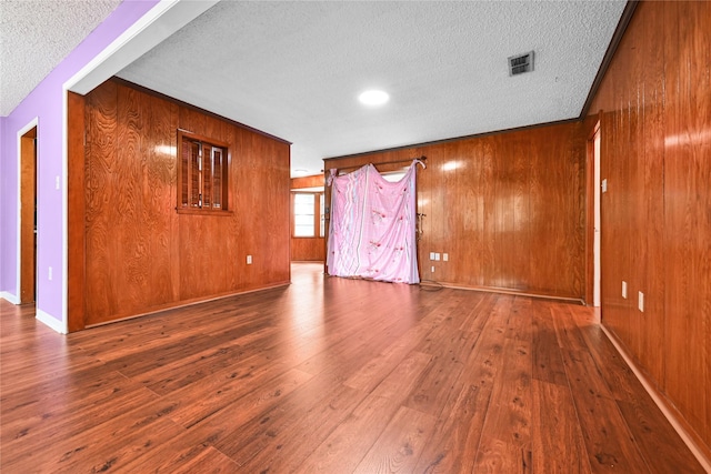 unfurnished room with a textured ceiling, hardwood / wood-style flooring, wooden walls, and baseboards