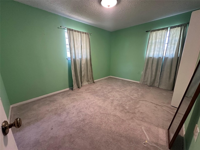 carpeted empty room with a textured ceiling, plenty of natural light, and baseboards