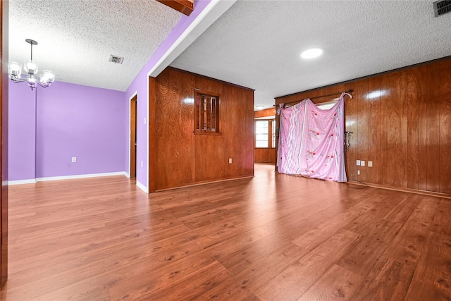 unfurnished living room with a textured ceiling, wood finished floors, a chandelier, wood walls, and baseboards