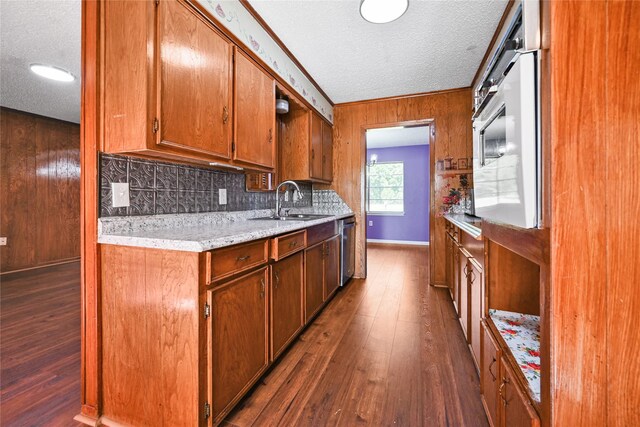 kitchen featuring a textured ceiling, a sink, dishwasher, dark wood-style floors, and wood walls