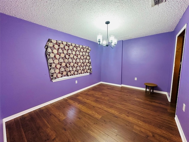 spare room with baseboards, visible vents, wood finished floors, a textured ceiling, and a chandelier