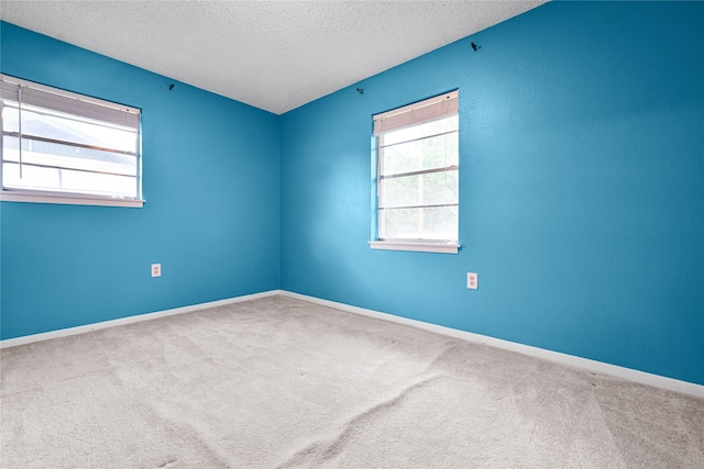 empty room featuring a textured ceiling, carpet flooring, and baseboards