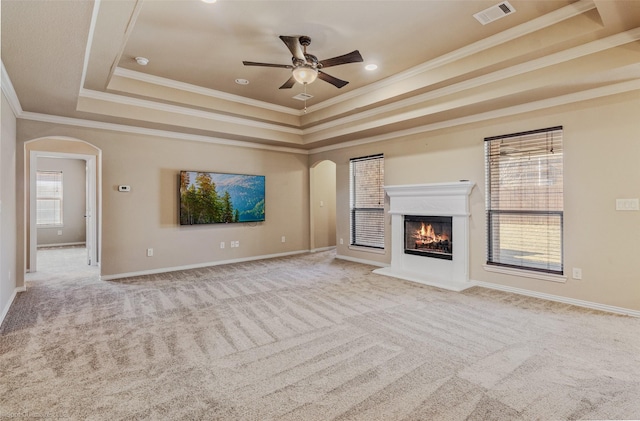 unfurnished living room with arched walkways, visible vents, a raised ceiling, carpet, and a glass covered fireplace