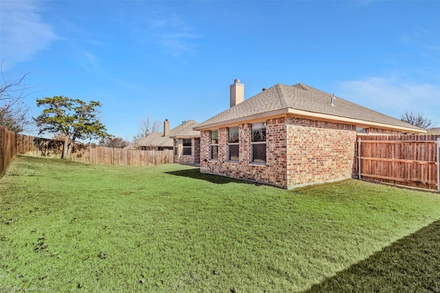 back of house with brick siding, a chimney, a shingled roof, a lawn, and a fenced backyard