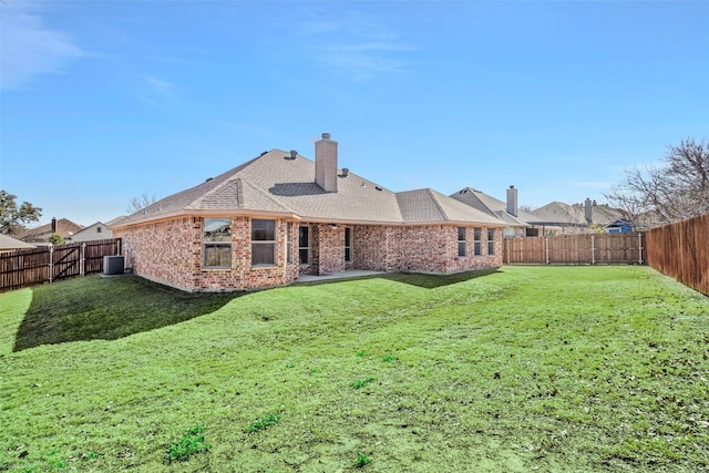 rear view of property featuring a yard, a fenced backyard, a chimney, and brick siding