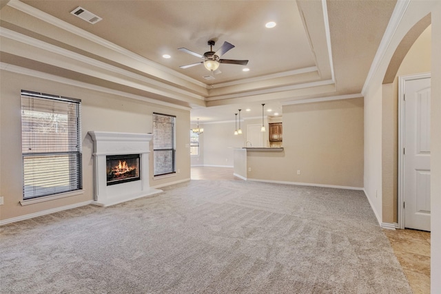 unfurnished living room with light colored carpet, ceiling fan with notable chandelier, visible vents, a lit fireplace, and a raised ceiling