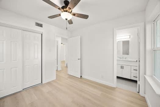 unfurnished bedroom with baseboards, visible vents, light wood-style flooring, ensuite bathroom, and a closet