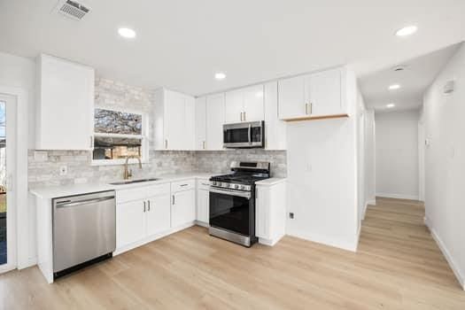 kitchen with light countertops, appliances with stainless steel finishes, a sink, and white cabinetry