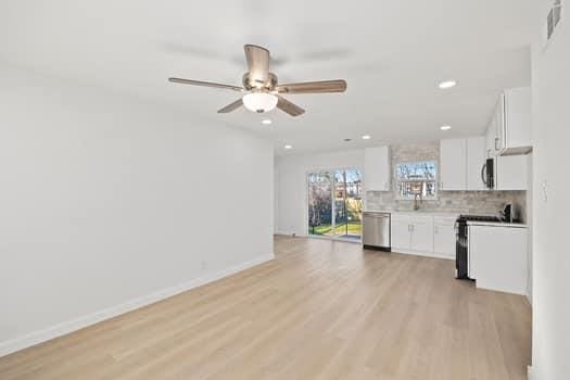 kitchen with stainless steel appliances, light countertops, backsplash, light wood-style floors, and white cabinetry