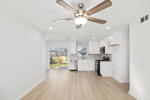 kitchen featuring light wood finished floors, appliances with stainless steel finishes, backsplash, and white cabinets