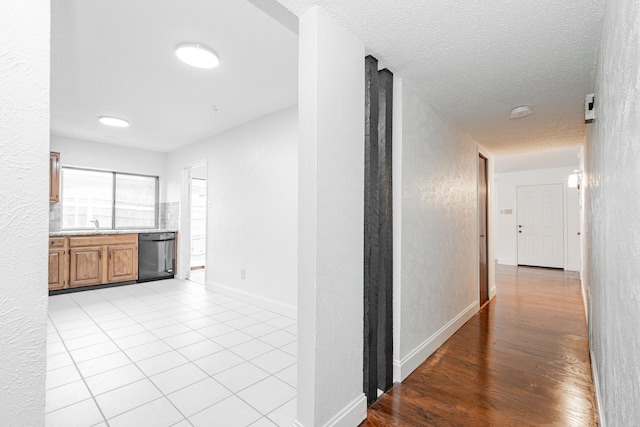 corridor featuring light tile patterned floors, baseboards, a textured ceiling, and a textured wall