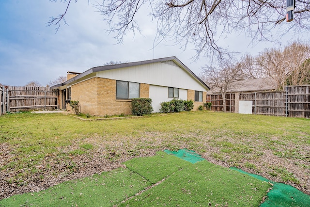 view of side of property with brick siding, a yard, a chimney, and a fenced backyard