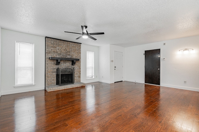 unfurnished living room with plenty of natural light, ceiling fan, wood-type flooring, and a brick fireplace