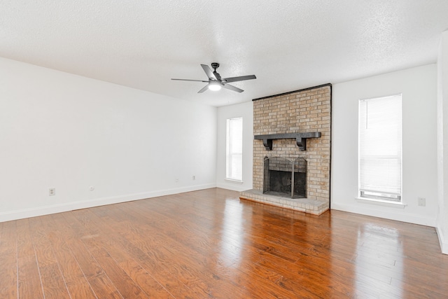 unfurnished living room with a brick fireplace, ceiling fan, a textured ceiling, wood finished floors, and baseboards