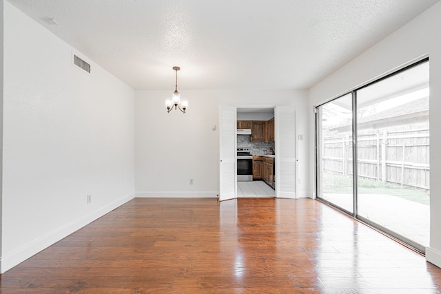 unfurnished living room with light wood finished floors, a textured ceiling, baseboards, and a notable chandelier