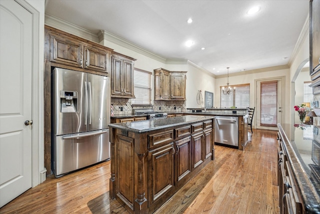 kitchen featuring a peninsula, a kitchen island, appliances with stainless steel finishes, decorative backsplash, and light wood finished floors