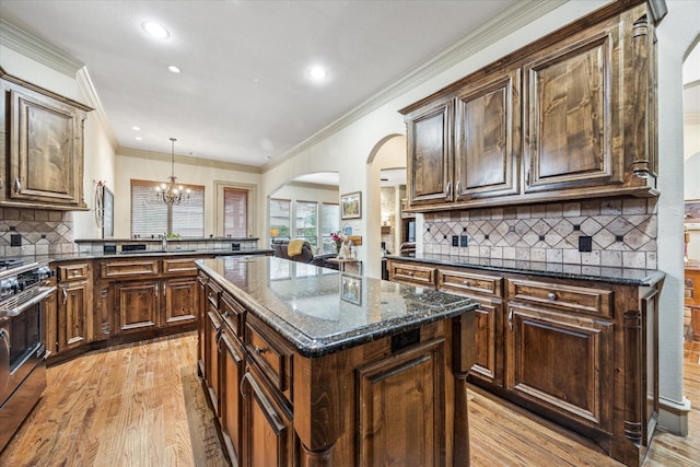 kitchen with dark stone counters, gas range, a center island, light wood-type flooring, and a chandelier