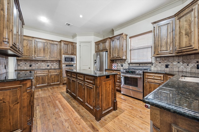 kitchen featuring tasteful backsplash, dark stone counters, stainless steel appliances, crown molding, and light wood-type flooring