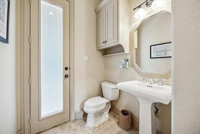 half bath with tile patterned flooring, baseboards, a sink, and toilet