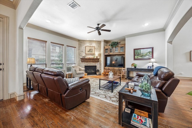 living room with arched walkways, visible vents, a stone fireplace, and wood finished floors