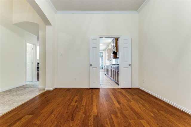 unfurnished room featuring baseboards, arched walkways, crown molding, and wood finished floors