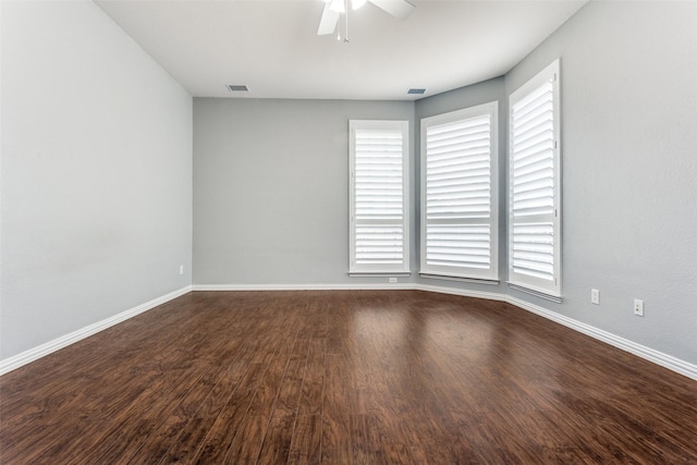 spare room with dark wood-style flooring, plenty of natural light, visible vents, and baseboards