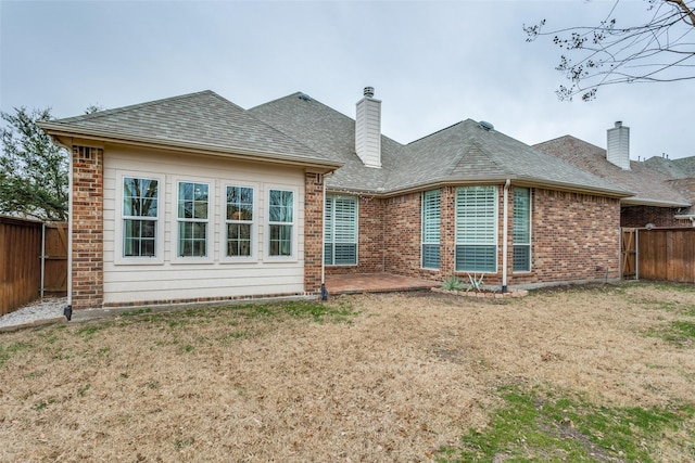 rear view of house with a yard, brick siding, a shingled roof, and a fenced backyard