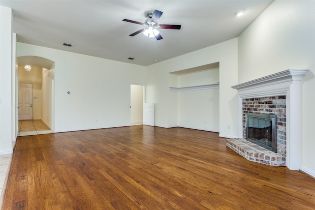 unfurnished living room featuring visible vents, arched walkways, a ceiling fan, wood finished floors, and a fireplace