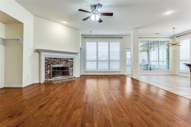 unfurnished living room with ceiling fan with notable chandelier, a fireplace, and wood finished floors