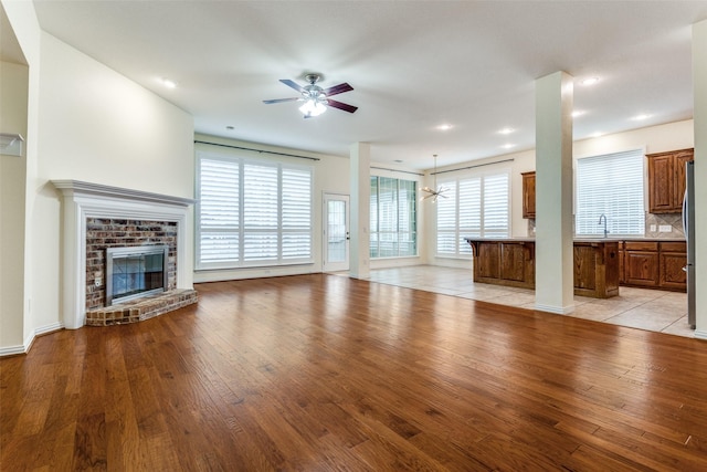 unfurnished living room featuring a sink, light wood-style flooring, a fireplace, and a ceiling fan