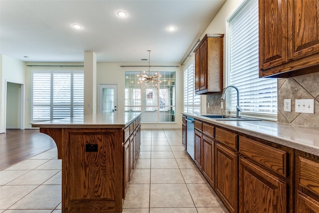 kitchen with light tile patterned floors, dishwasher, a center island, a sink, and backsplash