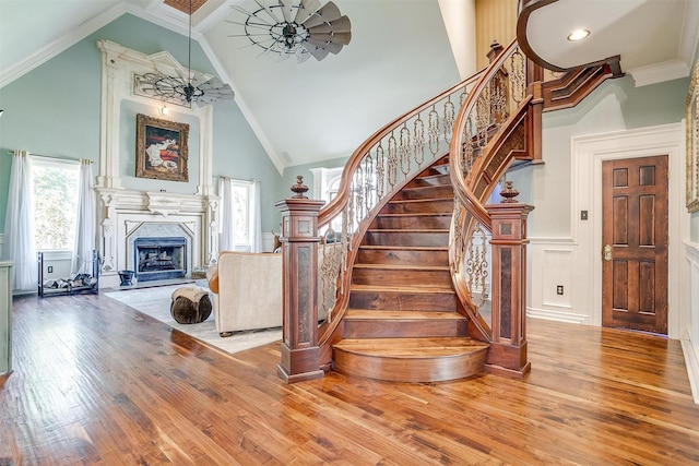 staircase with ornamental molding, a high end fireplace, ceiling fan, high vaulted ceiling, and hardwood / wood-style floors