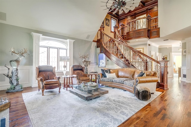 living room featuring a decorative wall, a high ceiling, wood finished floors, stairway, and wainscoting